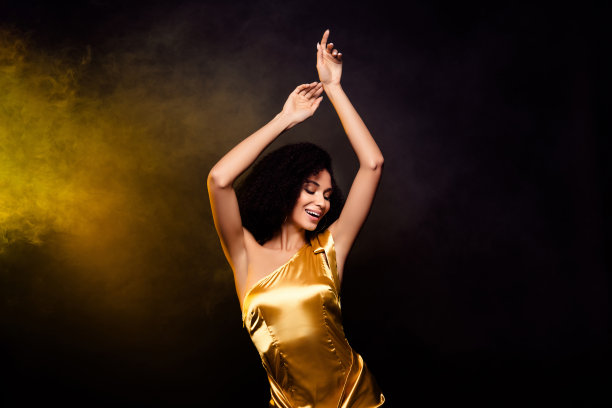 穿着金色裙子的优雅梦幻女士在黄色灯光背景下享受舞蹈的照片图片下载