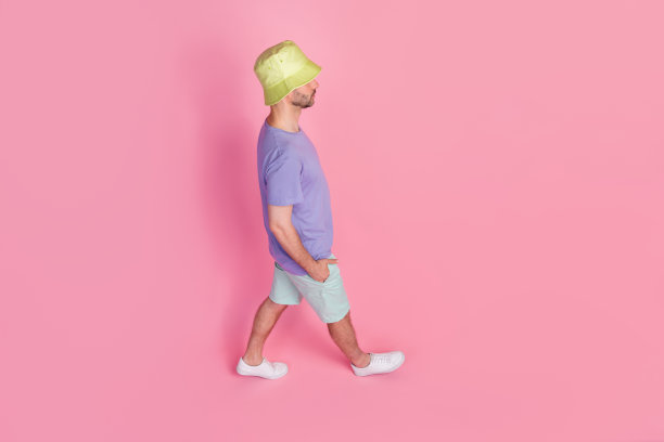 全身照片，高角度侧面视图，年轻男子穿着时尚的蓝色休闲装，走在粉色背景上，适合周末旅游。图片下载