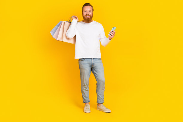 留着时髦胡子的男子拿着包、电话穿白色衬衫、牛仔裤、靴子的全长照片，背景为黄色图片下载