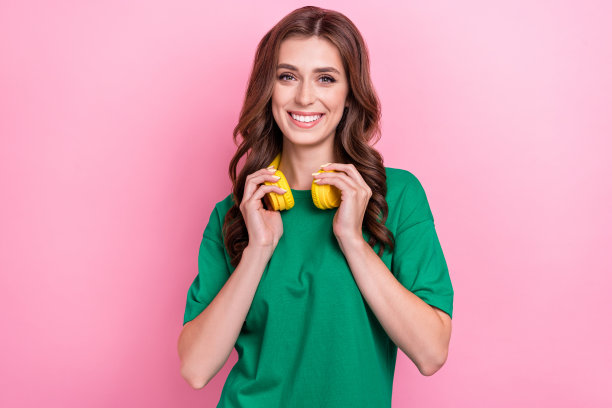 特写照片，漂亮可爱的女士穿着绿色时尚服装，佩戴耳机，脖子上挂着新设备，背景为粉色。图片下载