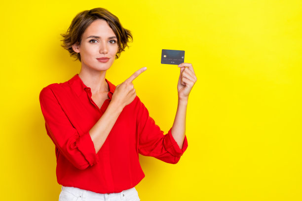 金发女孩经理的肖像照片，推荐新银行卡，手指指向无线支付，背景为黄色。图片下载