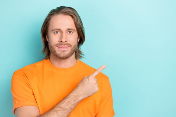 年轻帅气自信的男学生特写照片，手指指向空白处，正在使用在线购物应用，背景为蓝色。图片下载