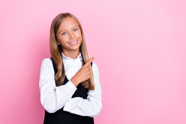特写照片，年轻可爱的女学生穿着校服，露出灿烂的笑容，长长的金发，手指指向空白处，背景为粉色。图片下载
