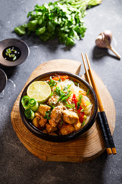 一碗玻璃或透明面条，上面放着亚洲风味的焦糖鸡胸肉，摆放在桌子上的竖版照片图片下载