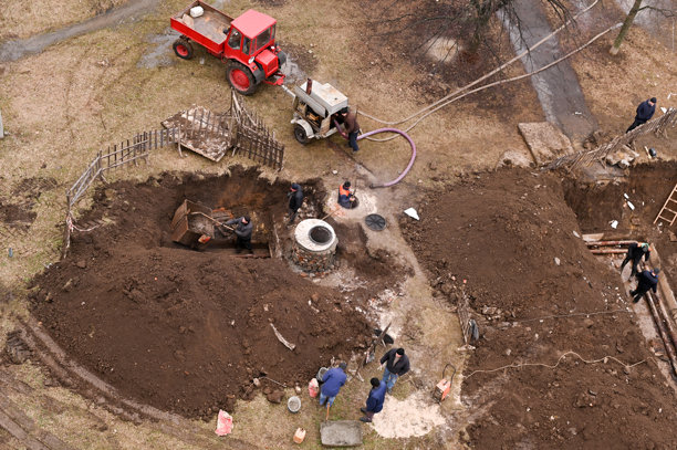 拖拉机带来了一个压缩机，用于从污水井中抽水。一组管道工在街上进行更换污水管道的工作。乌克兰哈科夫地区，洛佐瓦亚 - 2022年12月23日。编辑照片图片下载