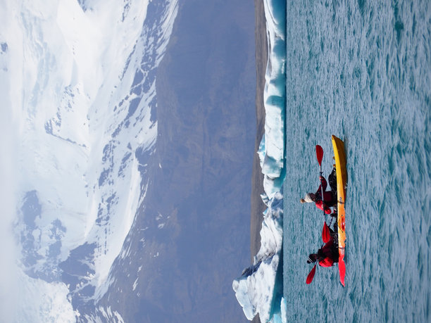 冰岛的杰古沙龙湖 - 2024年5月16日：照片展示了人们在清澈的冰川水域中划皮艇，背景是雪山和冰山。图片下载