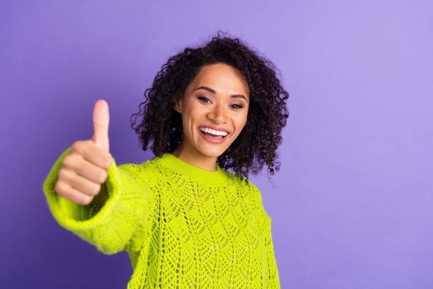 穿着绿色时尚针织毛衣的波浪卷发学生女孩的肖像照片，背景为紫色，展现积极的反馈。图片下载