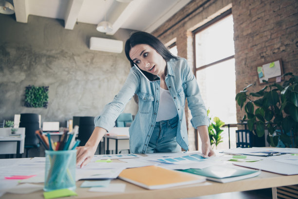 时尚的年轻女士在现代办公环境中穿着牛仔服，正在分析电话通话的照片肖像。图片下载