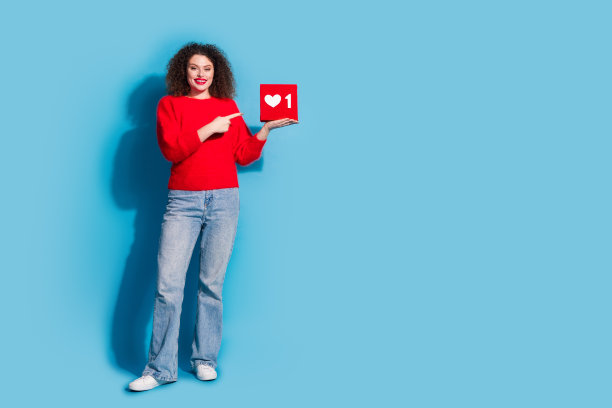 穿着时尚红色服装的漂亮年轻女孩手持社交媒体图标的全身照片，背景为蓝色。图片下载