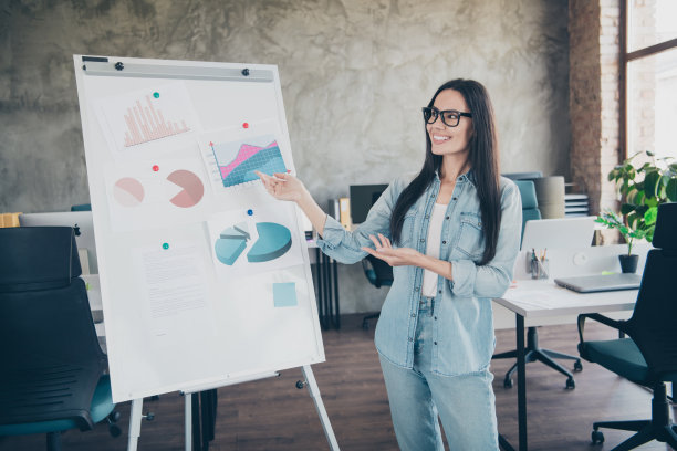 时尚年轻女性在现代办公环境中指着图表的照片肖像，穿着时尚的牛仔服装。图片下载