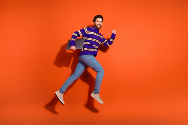 全身照片，英俊的年轻男子穿着时尚的紫色条纹服装，奔跑时手持笔记本电脑，背景为橙色。图片下载