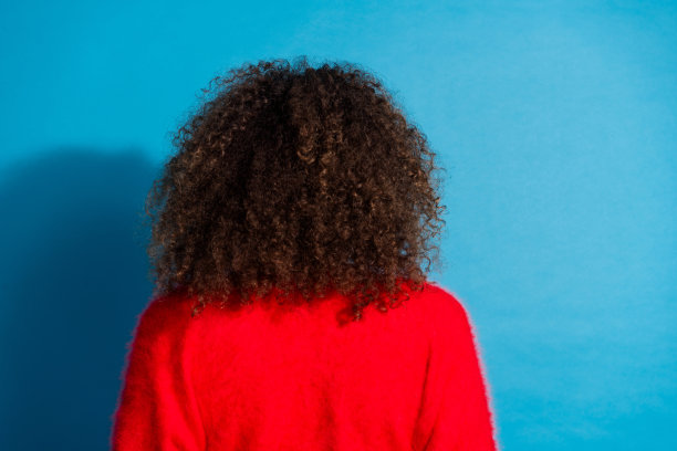 漂亮年轻女孩的照片肖像，展示了她的背面发型，穿着时尚的红色服装，背景为蓝色。图片下载