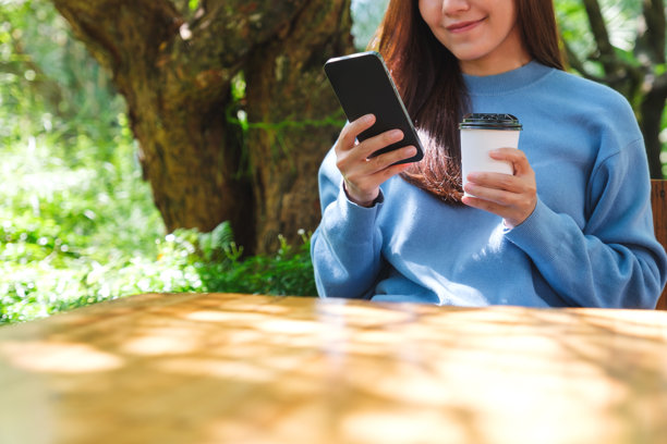 户外一位女性近距离使用手机并喝咖啡的照片图片下载