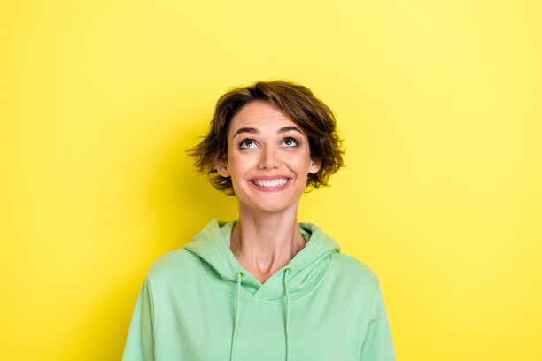 特写照片：一位穿着绿色衣服的兴奋女士，面带喜悦，目光投向空旷的空间，背景为黄色，价格低廉。图片下载