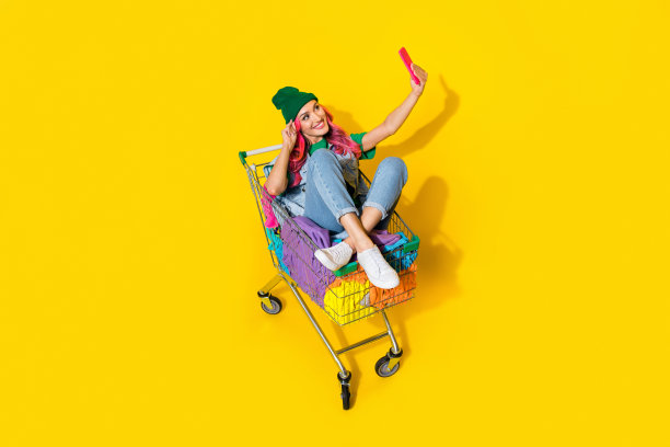 穿着牛仔背心的时尚迷人女孩在黄色背景下骑着衣物堆录制视频博客的全身照片图片下载