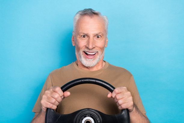 特写照片：一位有趣、时尚、快乐的老年退休男士在蓝色背景下，因试驾自己新车的速度而感到惊讶。图片下载