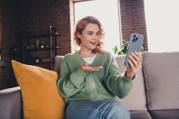 穿着绿色开衫的可爱女性在室内公寓房间使用现代设备进行视频通话的照片图片下载