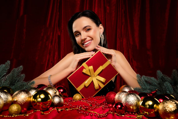穿着鸡尾酒服的富有迷人女士在红色天鹅绒背景前接受新年礼物的照片图片下载