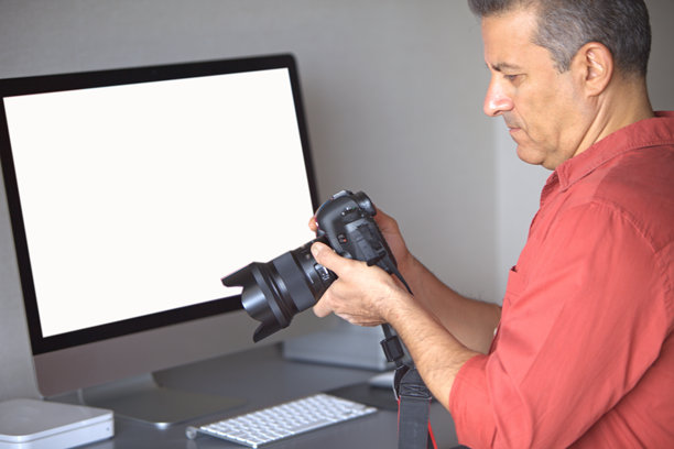 中年摄影师在家中将相机中的照片上传到电脑，白色屏幕。图片下载
