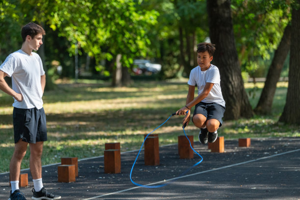 年轻男孩在户外跳绳，在教练的指导下，强调协调性和健身。照片突显了一个充满活力、有趣的训练课程，背景为自然开阔的环境。图片下载
