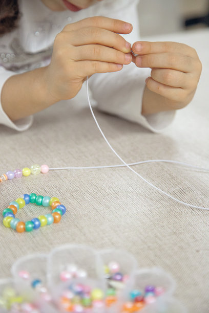 孩子的手特写，正在将五颜六色的珠子穿在绳子上，专注于制作手工手链。这张图片展现了创造力、精细运动技能和有趣的学习。图片下载