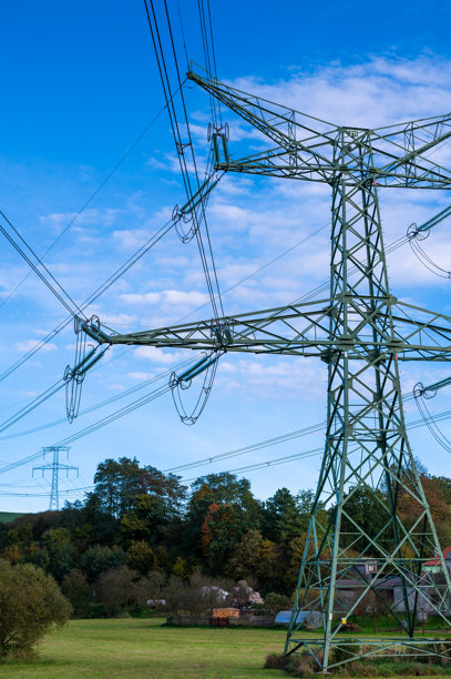 一幅风景照片，展示了电力线和输电塔延伸穿过开阔的田野，背景是丘陵和部分多云的天空。该图像捕捉了自然与工业的交汇，突显了基础设施在乡村中的作用。图片下载
