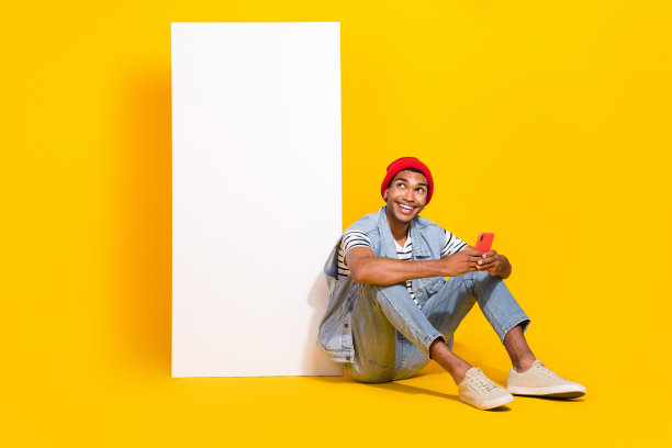 穿着牛仔服的迷人男孩在空旷的黄色背景下与电子设备聊天的全身照片图片下载