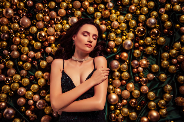 俯视照片中，一位惊艳的美丽女士躺在圣诞树上，金色球饰触碰着她的手，闭着眼睛。图片下载
