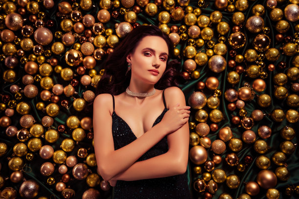 俯视照片中，一位迷人的漂亮女士躺着，手触碰金色圣诞节装饰品，感受着诱惑。图片下载