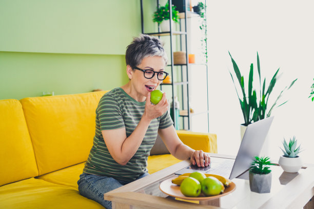 迷人的退休女士在室内房间里穿着绿色衣服吃苹果的午餐照片图片下载