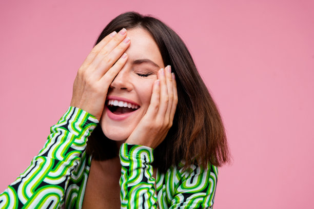 特写照片，迷人的女性穿着绿色衣服，手臂触碰脸庞，背景为粉色。图片下载