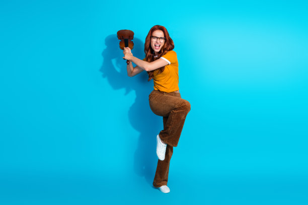 愤怒的年轻女音乐家穿着时尚服装，手持小提琴在蓝色背景下争斗的照片图片下载