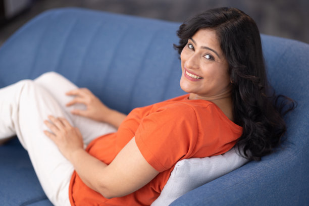 美丽的女人坐在家里的沙发上看着镜头的照片图片下载