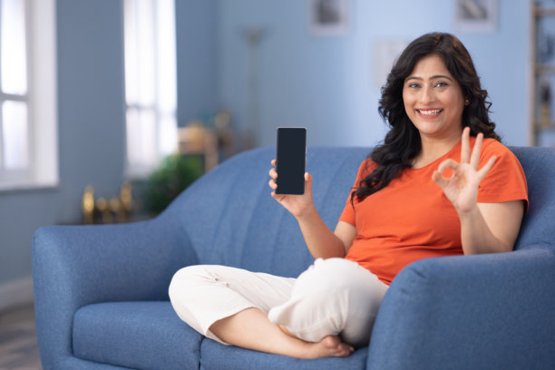 女人坐在家里的沙发上展示设备屏幕的照片图片下载