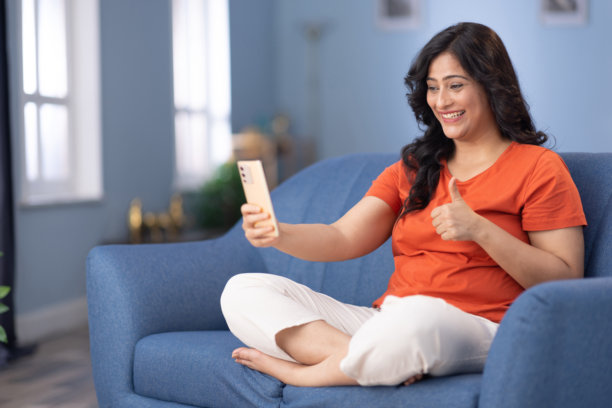 女人坐在家里的沙发上使用手机的库存照片图片下载