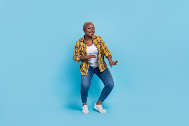 穿着格子衬衫的迷人女士在蓝色背景下微笑跳舞的全身照片图片下载