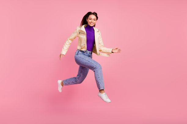 可爱的棕发女士穿着夹克、牛仔裤和靴子在粉色背景上奔跑的全身照片图片下载