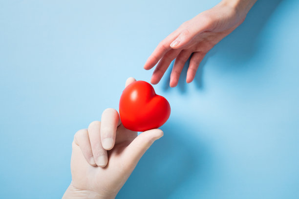 在蓝色背景上，两只手交换一个红色心形。象征着关怀、爱与健康，这张图片非常适合慈善、同情和医疗主题。图片下载