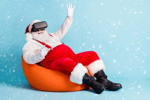 全身照片，退休老人试图触摸虚拟物体，完全沉浸在体验中，坐在橙色豆袋椅上，穿着红色圣诞老人服装，搭配吊带、太阳镜、帽子和靴子，背景为蓝色。图片下载