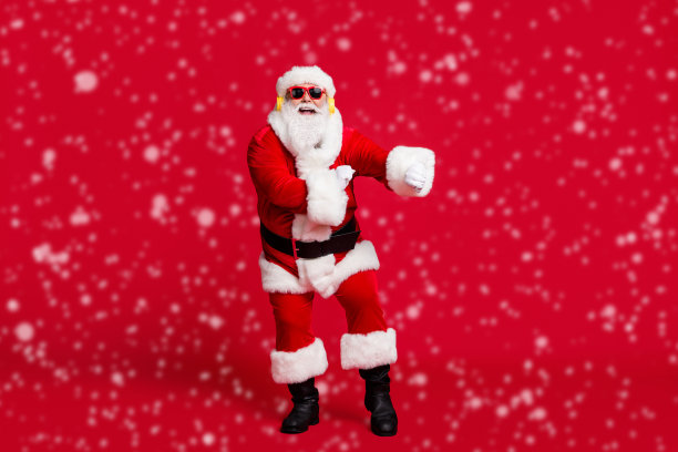 全身照片，退休老人，灰色胡须，搞笑舞蹈，手势，穿着圣诞老人服装，手套，外套，腰带，太阳镜，头饰，耳机，黑色靴子，背景为红色。图片下载
