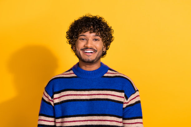 年轻帅气男子的照片肖像，面带灿烂微笑，穿着时尚的蓝色条纹衣服，背景为黄色。图片下载