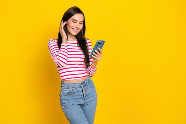 年轻可爱的女孩在黄色背景下微笑着，触摸着头发，使用手机进行网络摄像头拍摄的肖像照片。图片下载