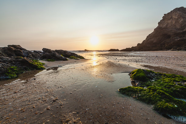 海滩照片捕捉到落日的余晖映照在湿润的沙滩和海岸边的小潮池上。图片下载