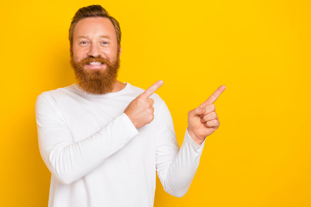 年轻帅气的红发男士在黄色背景上推荐专业应用，指向空白区域的特写照片图片下载