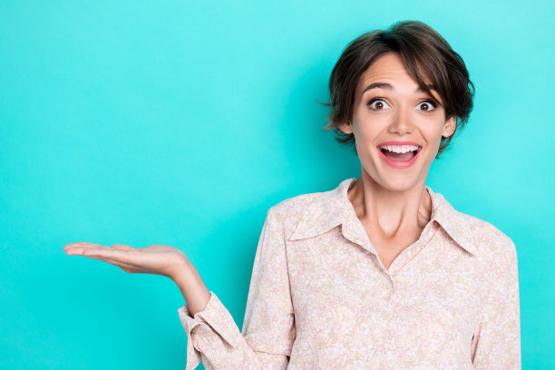 特写照片：年轻迷人、可爱完美的女性，因惊讶而无言，开心地手持新物品，背景为水绿色。图片下载