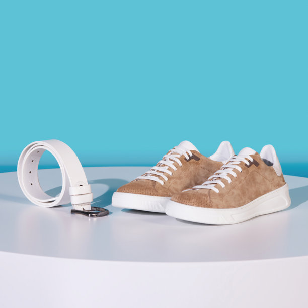 夏季鞋子和白色腰带，放在白色地面和蓝色背景上，拍摄于工作室。棕色绒面皮革运动鞋，配有白色鞋底和鞋带，静物照片。图片下载