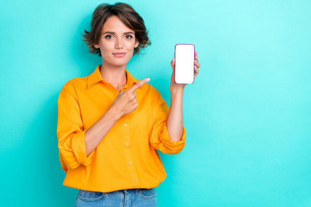 年轻可爱的女学生商人肖像照片，手持手机，手指指向空白屏幕，手机广告她的博客和Facebook，背景为青色。图片下载