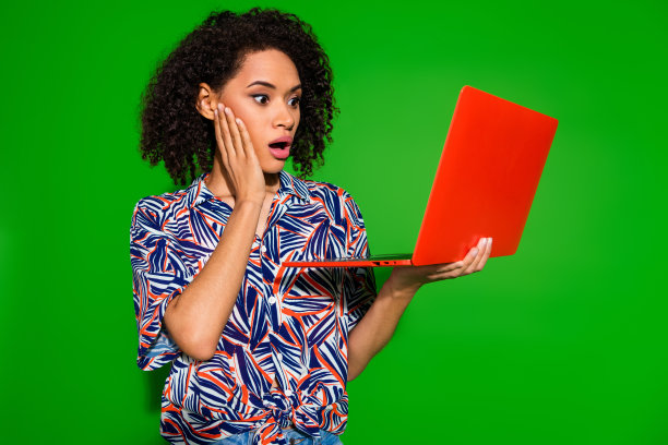 漂亮年轻女孩的照片肖像，手持笔记本电脑，惊讶的表情，穿着时尚多彩的服装，背景为绿色。图片下载