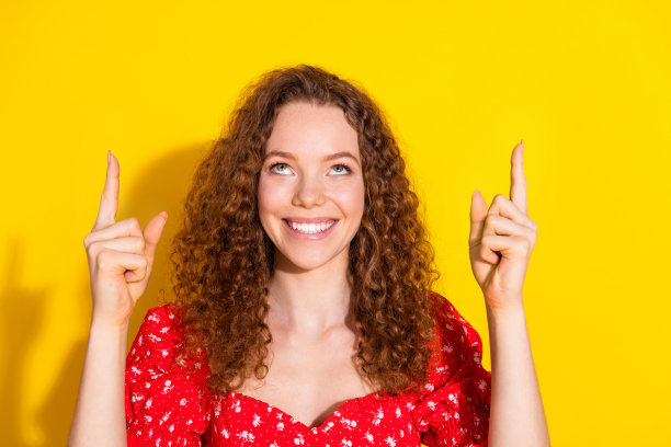 漂亮年轻女孩的照片肖像，指着向上看空旷的空间，穿着时尚的红色服装，背景为黄色。图片下载