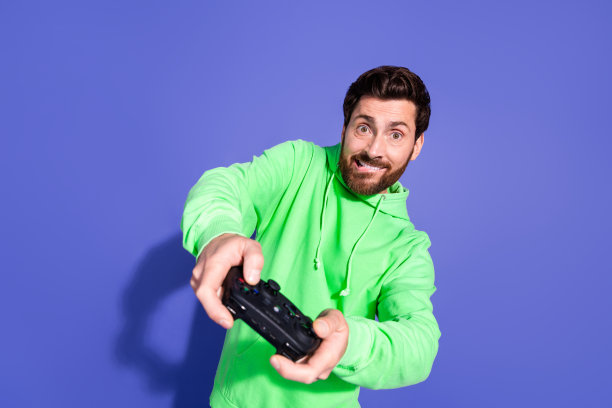 穿着绿色连帽衫的帅气成熟男子在紫色背景下使用游戏手柄玩游戏的照片肖像图片下载